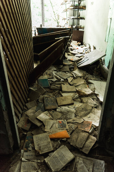 PRIPYAT, UKRAINE - AUGUST 15, 2019: dirty and abandoned classroom with books on floor in school 