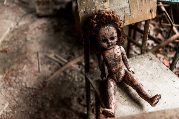 dirty and burnt baby doll on wooden chair in school 