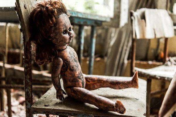 selective focus of dirty and burnt baby doll on wooden chair in school 