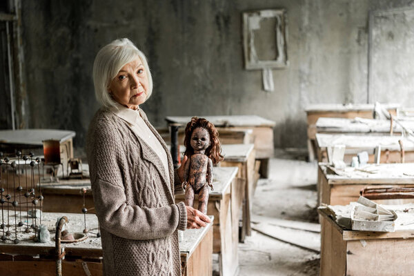 selective focus of retired woman with grey hair holding dirty baby doll 