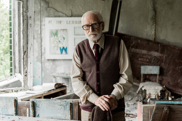 selective focus of retired man holding hat while standing in classroom 