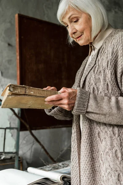 PRIPYAT, UKRAINE - AUGUST 15, 2019: retired woman with grey hair holding book in hands
