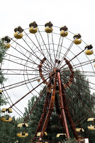 PRIPYAT, UKRAINE - AUGUST 15, 2019: abandoned and rusty carousel in amusement park with trees against sky 