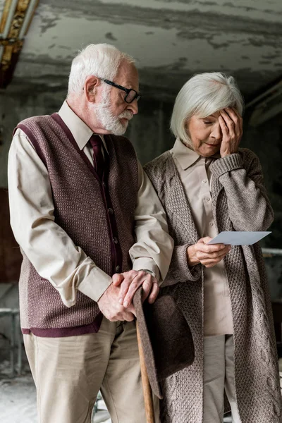 写真を持ちながら あごひげの夫の近くで顔に触れる引退した女性 — ストック写真