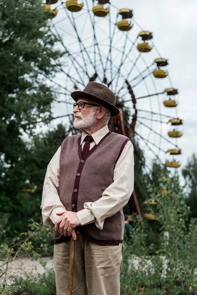 プリピャト ウクライナ 8月15 2019 観覧車のある遊園地で杖を持って歩く帽子の髭のシニア男性 — ストック写真