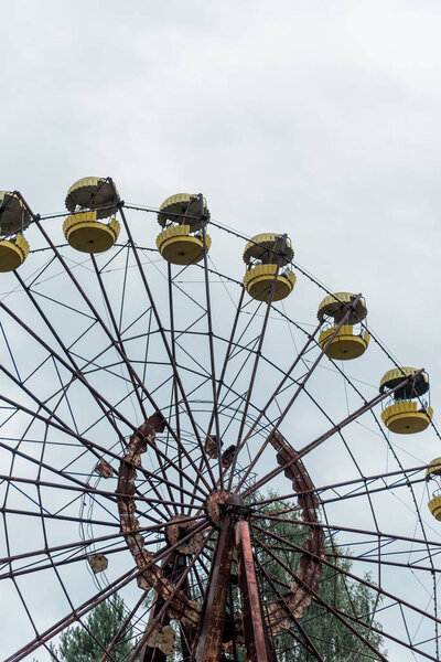 PRIPYAT, UKRAINE - AUGUST 15, 2019: abandoned and rusty ferris wheel in green amusement park against blue sky 