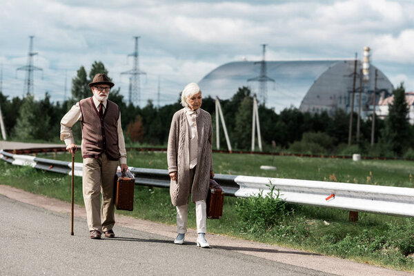 PRIPYAT, UKRAINE - AUGUST 15, 2019: senior man and woman walking with luggage near chernobyl reactor