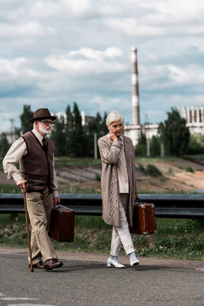 ПРИПЯТ, УКРАИНА - 15 августа 2019 года: мужчина и женщина старшего возраста ходят с багажом рядом с Чернобыльской АЭС
 