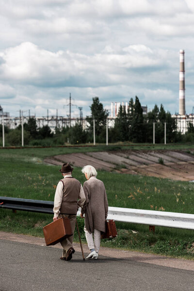 PRIPYAT, UKRAINE - AUGUST 15, 2019: back view of senior couple walking with baggage near chernobyl nuclear power plant 