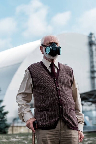PRIPYAT, UKRAINE - AUGUST 15, 2019: senior man in protective mask standing near abandoned chernobyl reactor 
