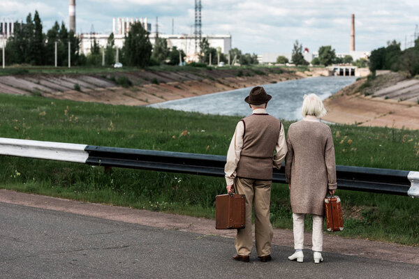 PRIPYAT, UKRAINE - AUGUST 15, 2019: back view of senior couple with baggage near chernobyl nuclear power plant 