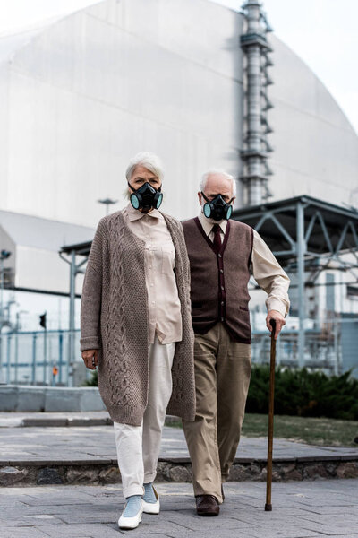 PRIPYAT, UKRAINE - AUGUST 15, 2019: senior couple in protective masks standing near abandoned chernobyl reactor 