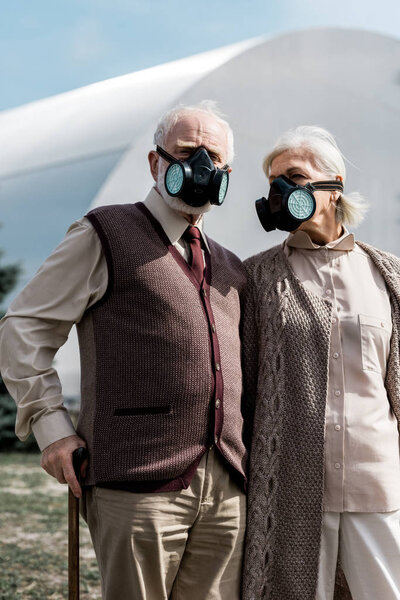 PRIPYAT, UKRAINE - AUGUST 15, 2019: senior husband and wife in protective masks standing near abandoned chernobyl reactor 