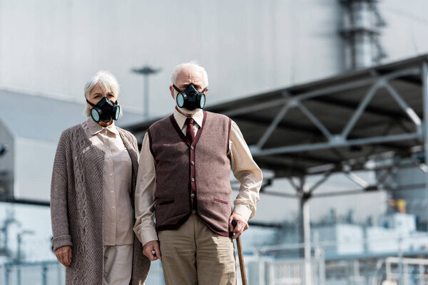 ПРИПЯТ, УКРАИНА - 15 августа 2019 года: пожилая женщина и мужчина в защитных масках стоят возле заброшенного Чернобыльского реактора
 