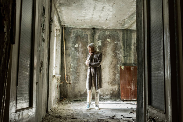 upset senior woman standing in empty and dirty room 