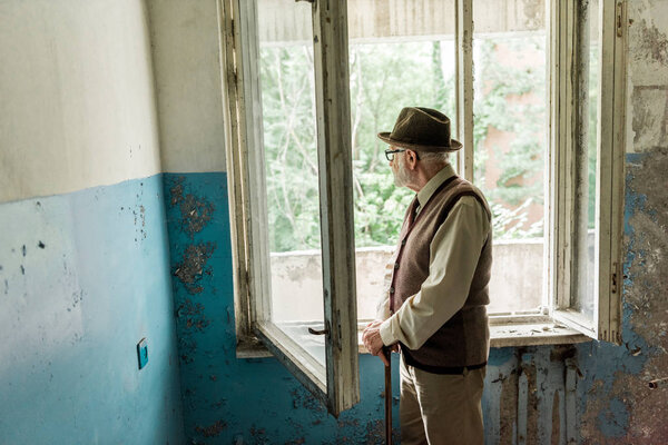 sad senior man standing in empty room in chernobyl 