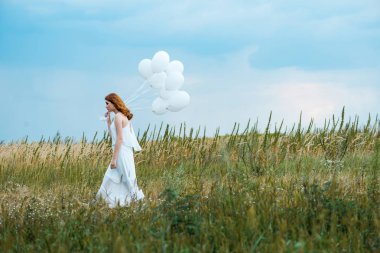 side view of redhead woman holding balloons in field  clipart