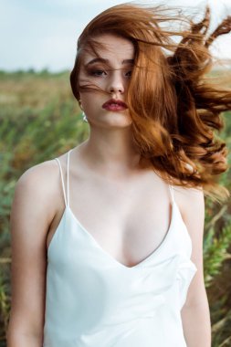selective focus of pretty redhead woman in white dress looking at camera  clipart