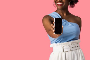 pembe izole boş ekran ile akıllı telefon tutan neşeli afrikalı amerikalı kız kırpılmış görünümü 