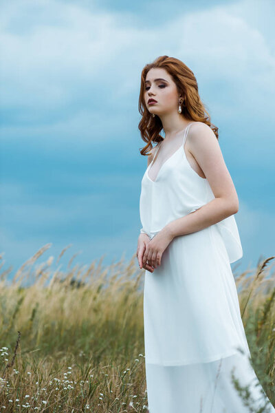 upset and pretty young woman in dress standing in field 