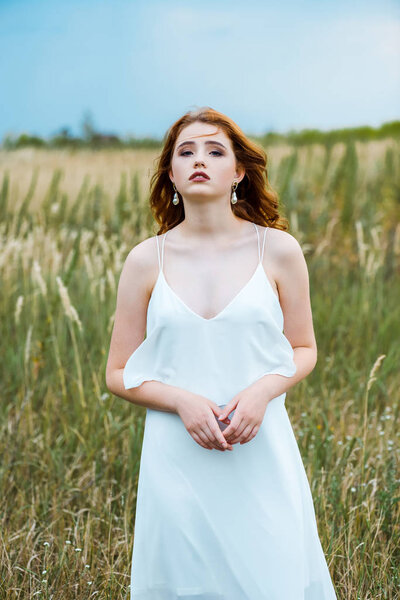 young redhead woman in white dress standing in field 