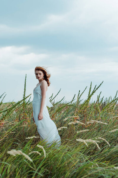 selective focus of redhead woman in white dress looking at camera 