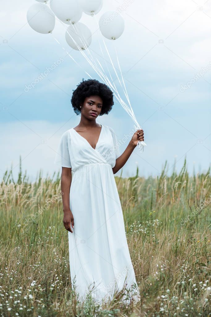 attractive african american girl in dress holding balloons in field 