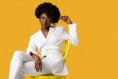 krásná Africká Američanka seděla na žlutém křesle izolovaná na oranžovém 