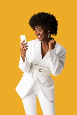 mutlu kıvırcık afrikalı amerikalı kadın akıllı telefon bakıyor ve turuncu izole gesturing 