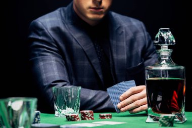 KYIV, UKRAINE - AUGUST 20, 2019: cropped view of man holding playing cards near poker chips isolated on black  clipart
