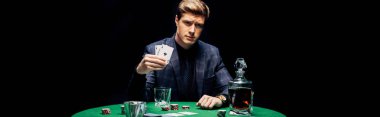 KYIV, UKRAINE - AUGUST 20, 2019: panoramic shot of handsome man holding playing cards near alcohol drink isolated on black  clipart
