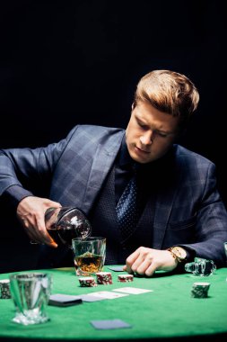 KYIV, UKRAINE - AUGUST 20, 2019: selective focus of man pouring whiskey in glass near playing cards isolated on black  clipart