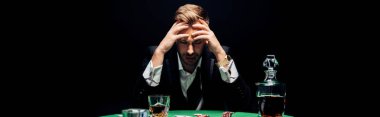 panoramic shot of sad man sitting near poker table isolated on black  clipart