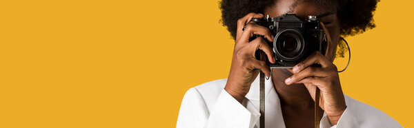 панорамный снимок кудрявой африканской женщины, покрывающей лицо во время съемки изолированного на оранжевом
 