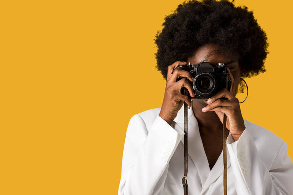 curly african american girl covering face while taking photo isolated on orange 