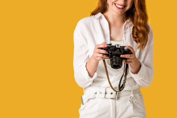 cropped view of happy redhead girl holding digital camera isolated on orange 