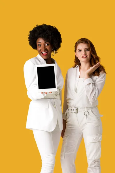 欢快的红发女孩手势接近非洲美国妇女拿着数字平板电脑与空白屏幕隔离在橙色 — 图库照片