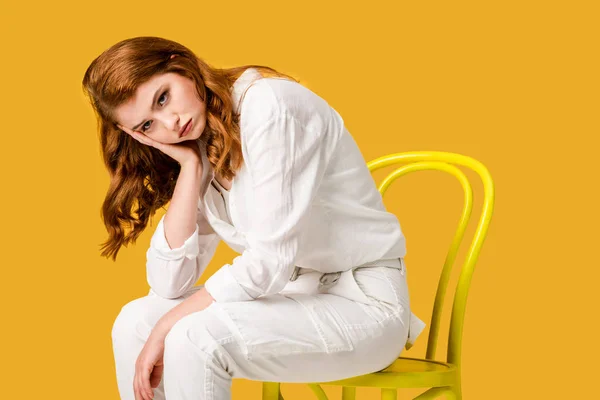 悲伤的红发女孩坐在黄色的椅子上孤立橙色 — 图库照片