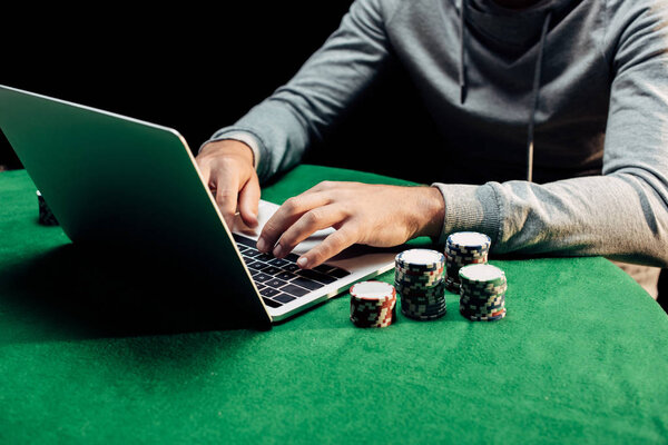cropped view of man typing on laptop near poker chips 