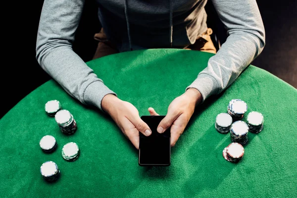 siyah poker yongaları yakınında boş ekran ile akıllı telefon tutan adam kırpılmış görünümü 