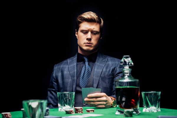 KYIV, UKRAINE - AUGUST 20, 2019: selective focus of man holding playing cards near alcohol drink isolated on black 