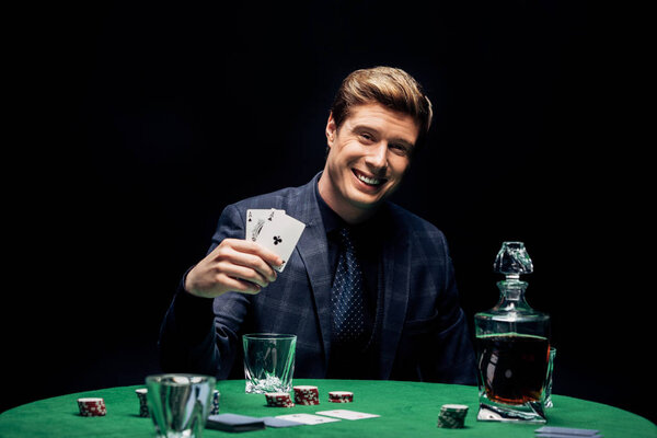 KYIV, UKRAINE - AUGUST 20, 2019: selective focus of happy man holding playing cards near alcohol drink isolated on black 