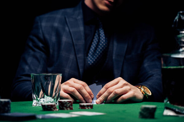 КИЕВ, УКРАИНА - 20 августа 2019 года: обрезанный вид человека, держащего игральные карты возле фишек для покера на черном
