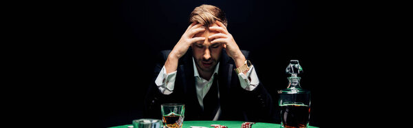панорамный снимок грустного человека, сидящего возле покерного стола, изолированного на черном
 