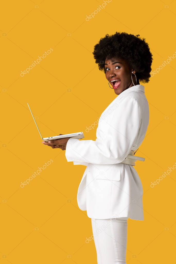 excited african american girl using laptop isolated on orange 