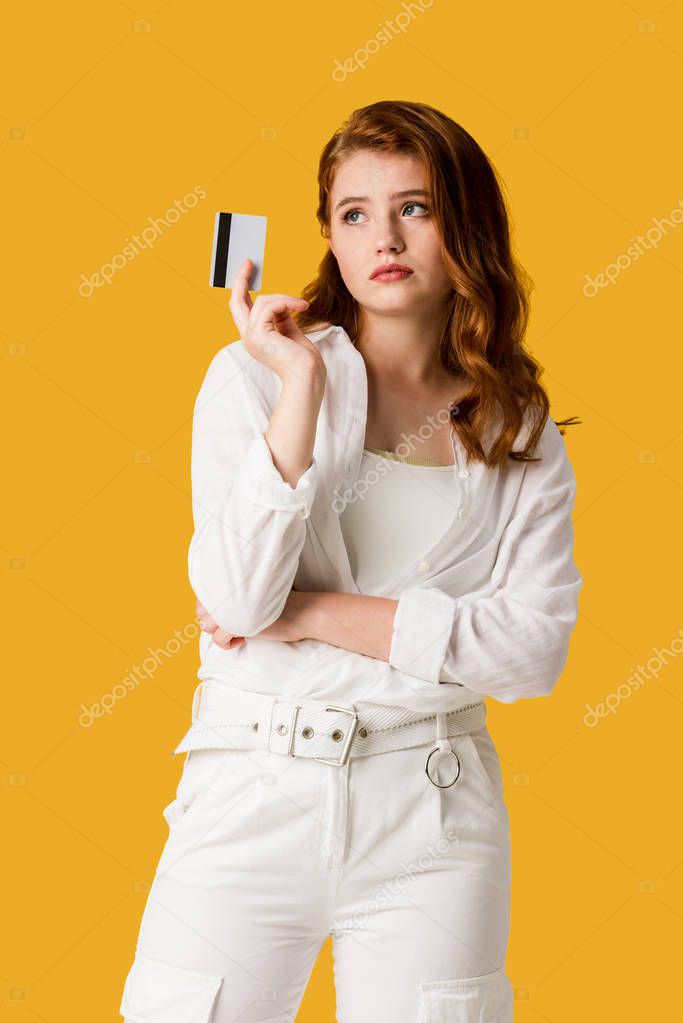 pensive girl holding credit card isolated on orange 