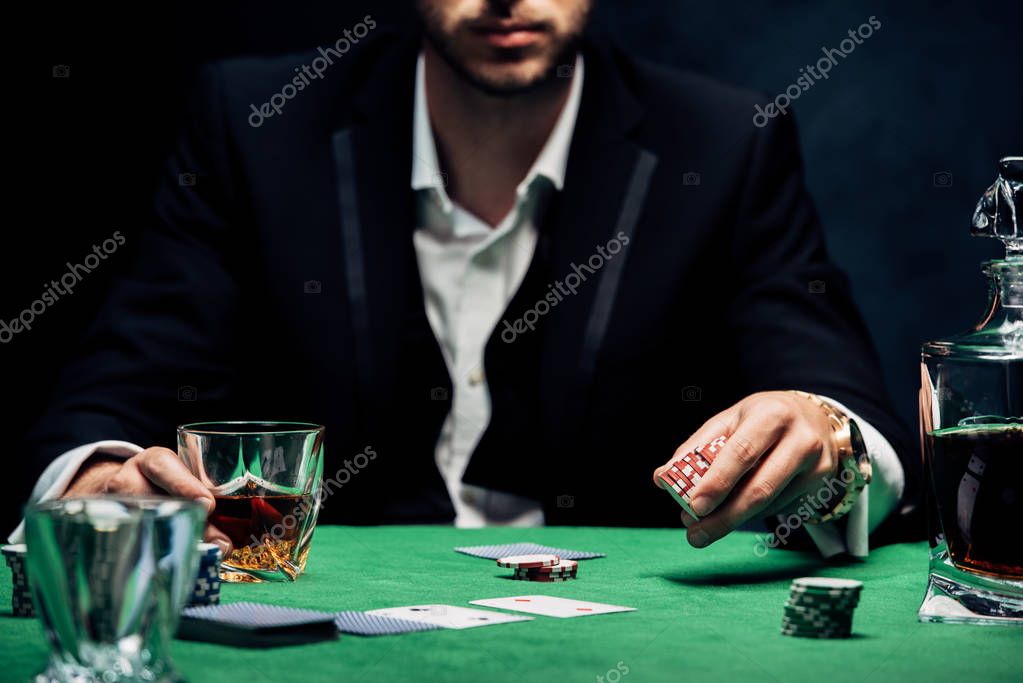 Cropped view of man holding poking chips and glass with alcohol on black with smoke