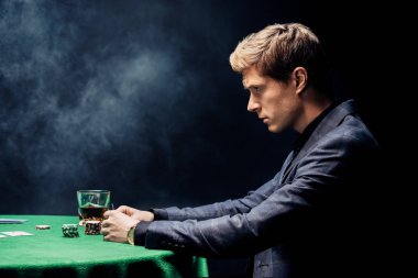 Siyah üzerine dumanla poker oynayan yakışıklı adamın yan görünüşü 