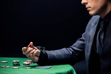 KYIV, UKRAINE - AUGUST 20, 2019: cropped view of man holding poker chip isolated on black  clipart