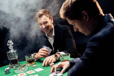 Kyiv, Ukrayna - 20 Ağustos 2019: Poker oynayan neşeli bir adamın seçici odak noktası yakın arkadaşı ve siyah üzerine siyah fişler duman 